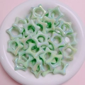 Dettaglio macro di perline acriliche a stella verde chiaro con riflessi iridescenti - Verde