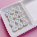 Detail of five pearlescent white heart beads with iridescent faceted centers in a ceramic tray - Clear White
