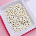 Close-up of white donut-shaped alloy beads for DIY jewelry making in a ceramic tray - Off-white