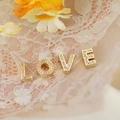 Close-up of gold LOVE letter charms with pavé cubic zirconia on white lace fabric - Gold A Style (PJ0229)