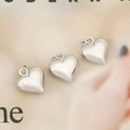 Three polished silver heart pendants with loops on a minimalist aesthetic background - Silver