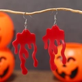 Gotische blutrote Acryl-Ohrringe an Zweig mit Halloween-Kürbissen im Hintergrund - Rot