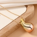 Close-up of a polished gold teardrop pendant on a sleek snake chain over a wooden base - Champagne KC Gold