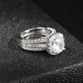 Detailed close-up of a halo pavé ring with a round center stone on a dark base - US 5 / White