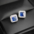 Elegantes aretes cuadrados de zafiro azul con halo de plata en un joyero de cuero negro - Azul