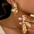 Primer plano de pendientes dorados con forma de concha y textura metálica martillada - Estilo Martillado de Pétalos Abstractos / Dorado