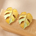 Elegant gold monstera leaf earrings with yellow and green enamel on a textured stand - Yellow Gold Monstera Leaf / Yellow