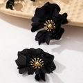 Close-up of black floral earrings with gold stamens on a white textured background - Black