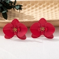 Nahaufnahme leuchtend roter Orchideen-Ohrringe mit goldenen Details auf Keramikteller - Rosenrote Ohrringe