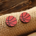 Macro detail of round wooden basketball earrings resting on textured burlap fabric - Basketball Style (WEH4172)