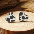 Macro shot of heart-shaped wooden earrings with black and white cow print on a rustic wood base - Cow Print (WEH4164)