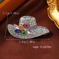 Macro detail of hat-shaped brooch with colorful rhinestones on brown silk background - White K Gold