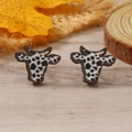 Primer plano de pendientes con estampado de vaca sobre fondo de madera rústica y hojas - Estilo Estampado Vaca Negro (WEH4311)