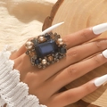 Baroque style ring with large blue gemstone and pearls on a textured wooden background - Ink Blue Antique Gold (Ring)
