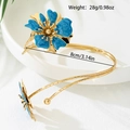 Golden open arm cuff bracelet with vibrant blue enamel flower and carved texture details - Blue