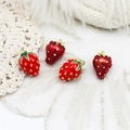 Detailed macro shot of red enamel strawberry charms with gold plating on lace fabric - Large Red Strawberry Style / Red