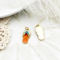 Detailed macro view of colorful enamel flip-flop pendants on white lace and feather - Orange Slipper