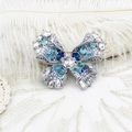 Elegante spilla a farfalla in argento con zirconi blu su uno sfondo di pizzo bianco - Farfalla Acquamarina
