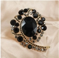Dettaglio macro di una spilla floreale vintage dorata con strass neri e pietra centrale - Nero