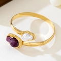 Detailaufnahme der goldenen Manschette mit unregelmäßigen weißen und lila Steinen - Armreif