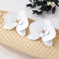 Detail view of 3D matte white orchid earrings with golden stamens on a textured tray - White