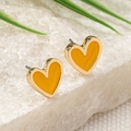 Macro detail of heart-shaped gold stud earrings with yellow enamel on a white stand - Yellow