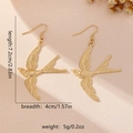 Golden swallow bird drop earrings in minimalist flying pose on textured beige background - Swallow Design (E1868-Little Swallow) / Gold
