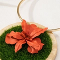 Macro shot of an orange metal flower pendant on a minimalist gold choker on a moss stand - Orange