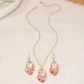 Nahaufnahme von gesichtsförmigem Goldschmuck-Set mit echten rosa getrockneten Blüten - Abstraktes Gesicht Rote Blume