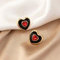 Elegantes pendientes de corazón dorado con esmalte negro y gema roja sobre fondo de seda - Negro