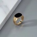 Macro shot of gold signet ring with black oval enamel face on white marble background - Gold