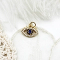 Detailed close-up of 18K gold evil eye charm with micro-pave crystals on white lace - Eyelash Hollow Zirconia Eye
