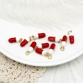 Macro shot of red and white enamel capsule charms with golden jump rings for DIY jewelry - Red Pill
