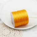 Close-up of golden elastic jewelry thread for DIY beading on a decorative white dish - Yellow 60m/Roll