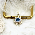 Macro shot of 18K gold evil eye charm with blue core on a white feather background - Evil Eye