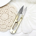 Golden U-shaped sewing thread snips shown on a white lace and plush background texture - Thread Snips Random Color