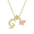 Detalle de un collar de oro con una letra G de circón y un colgante de planeta corazón rosa - Letra G