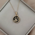 Detailed close-up of a gold Scorpio coin pendant with black enamel on a silk fabric - Gold-Scorpio