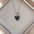 Detailed close-up of a heart-shaped black pendant necklace on champagne silk - Black