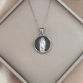 Nahaufnahme der silbernen Jungfrau Maria Guadalupe Kette auf einem Seidenhintergrund - Gelb