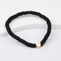 Detail of bohemian black heishi beads bracelet with a golden heart charm on a white stand - Black