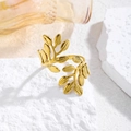 Detalle de anillo abierto dorado con diseño de hojas de olivo sobre piedra blanca - Abrazo Floral Dorado