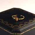 Detailansicht eines goldenen Wassertropfen-Rings mit Wellenkante auf einer Schmuckschatulle - Milchweiß Stil (R00027W)