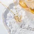 Close-up of a golden butterfly necklace featuring white zircon stones on a glass surface - Hollow Butterfly Necklace / White