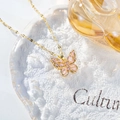 Close-up of gold butterfly necklace with pink crystals on crackled glass surface - Hollow Butterfly Necklace / Pink
