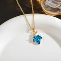 Detail of a vintage gold necklace featuring a faceted blue maple leaf pendant on a white plate - Blue