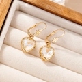 Detailed close-up of heart-shaped crystal earrings with golden floral accents on velvet - Mocha White