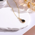 Macro detail of gold teardrop necklace with black pear gem on elegant stone display - Black