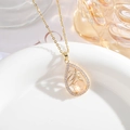 Détail macro du pendentif goutte doré avec pierre champagne et nœud serti de zircons - Blanc crème