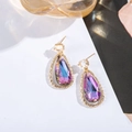 Macro detail of teardrop earrings featuring iridescent purple crystal in gold lace setting - Pink Purple